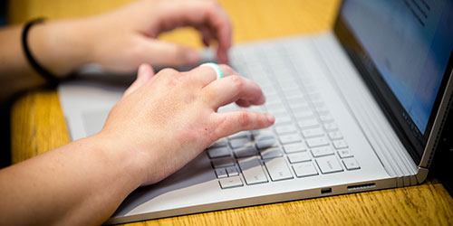 Close view of student typing on a laptop for their online course.