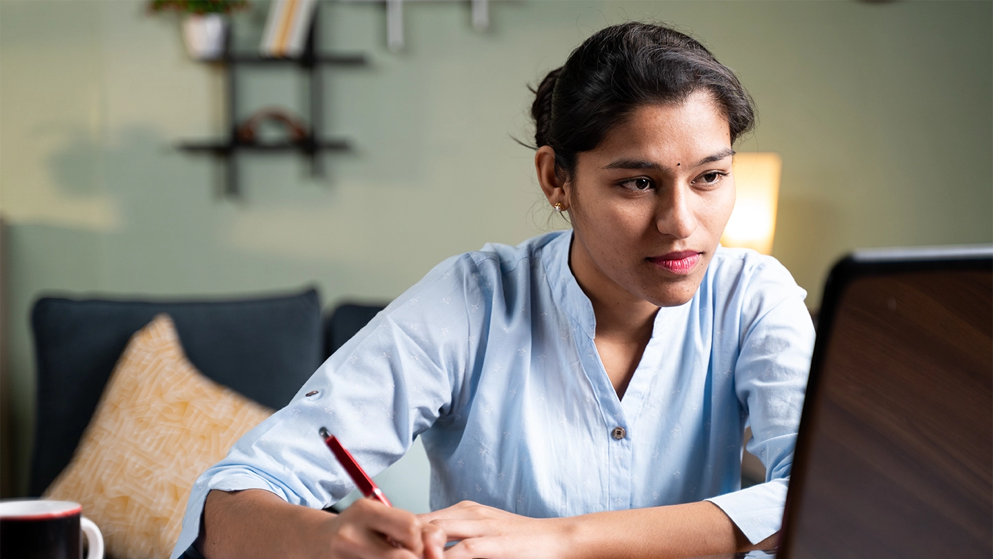 Online student taking notes while reading her laptop.