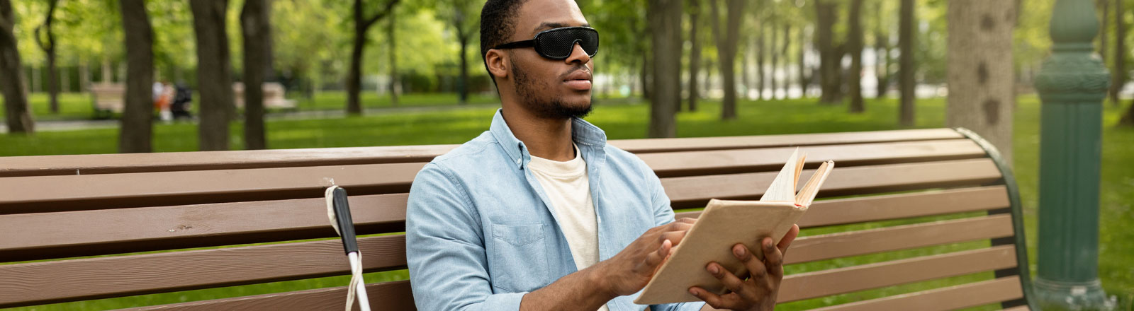 Visually impaired man sitting on park bench.
